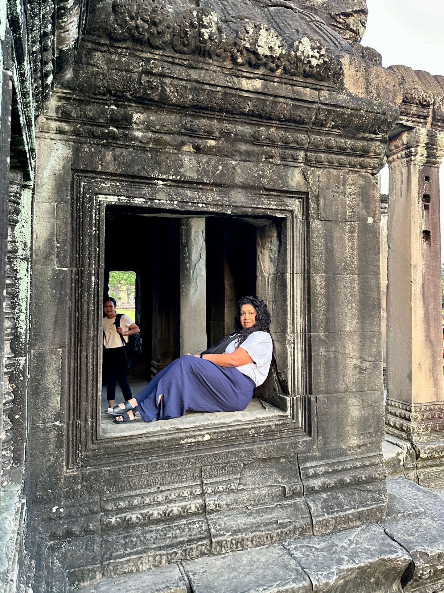 nishi visiting angkor wat, sat on a window ledge looking into the camera and view beyond