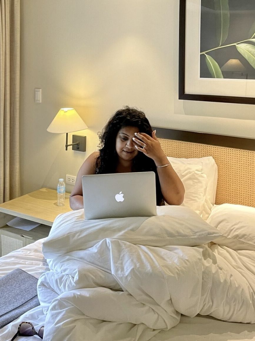 Nishi in a hotel bed sitting up using her laptop