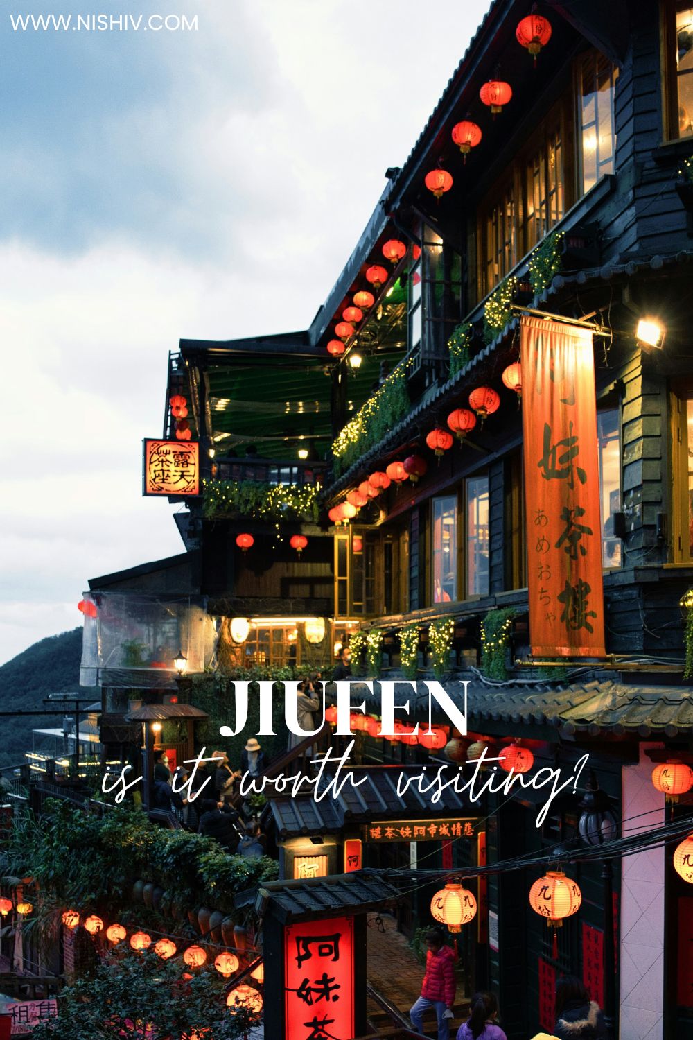 Evening view of Jiufen Old Street with glowing red lanterns lining traditional wooden buildings. Text overlay reads JIUFEN is it worth visiting while warm lights illuminate the narrow hillside walkway.