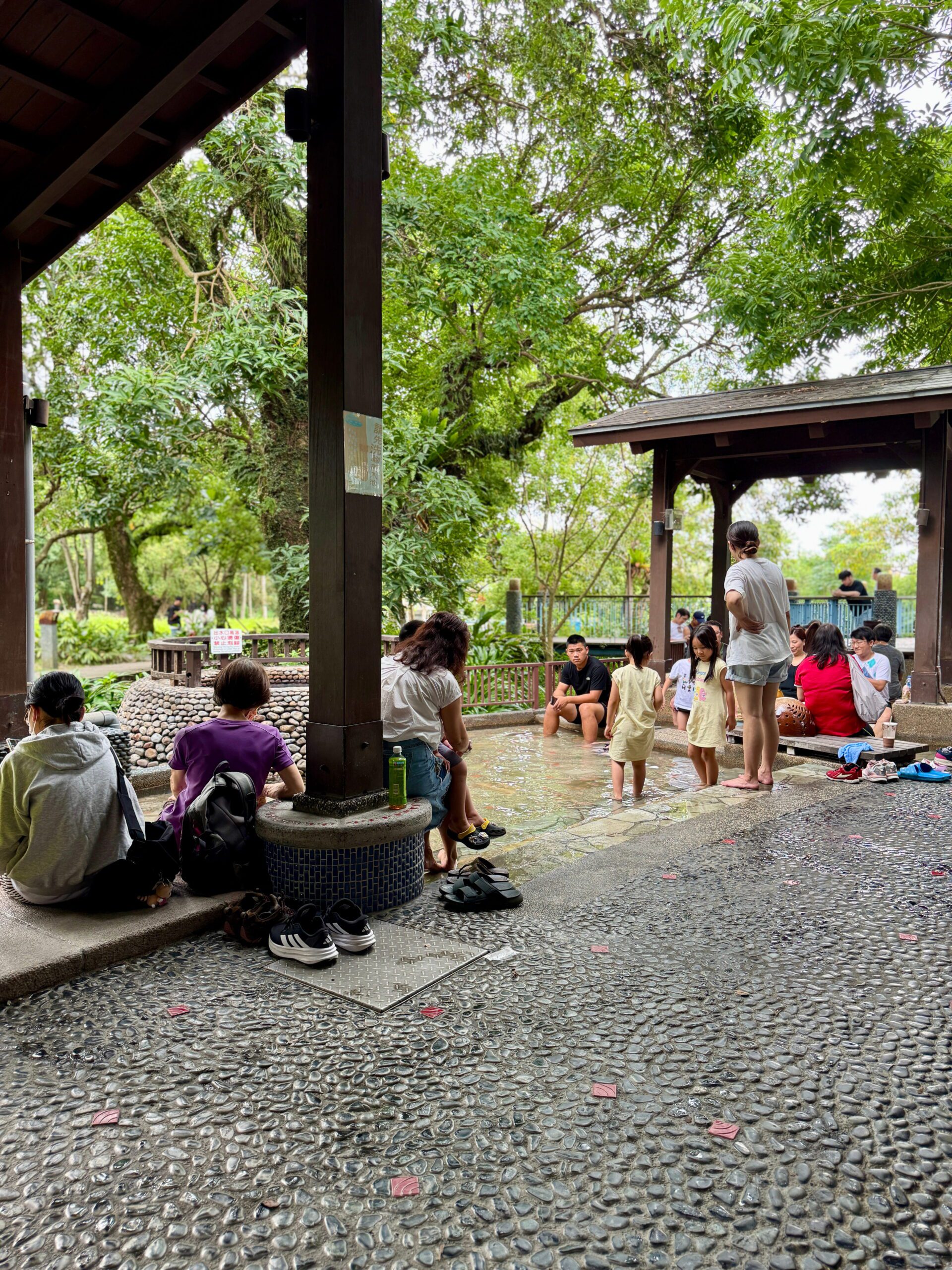 Group of visitors seated around a covered outdoor foot soaking pool enjoying the communal atmosphere at Jiaoxi hot springs park