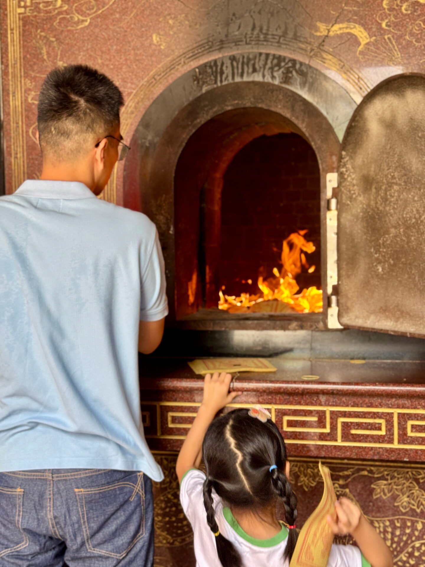 A man and a child stand in front of a temple furnace placing paper offerings into the fire as part of a traditional ritual at Sanfong Temple. Experiencing local customs is one of the meaningful things to do in Kaohsiung