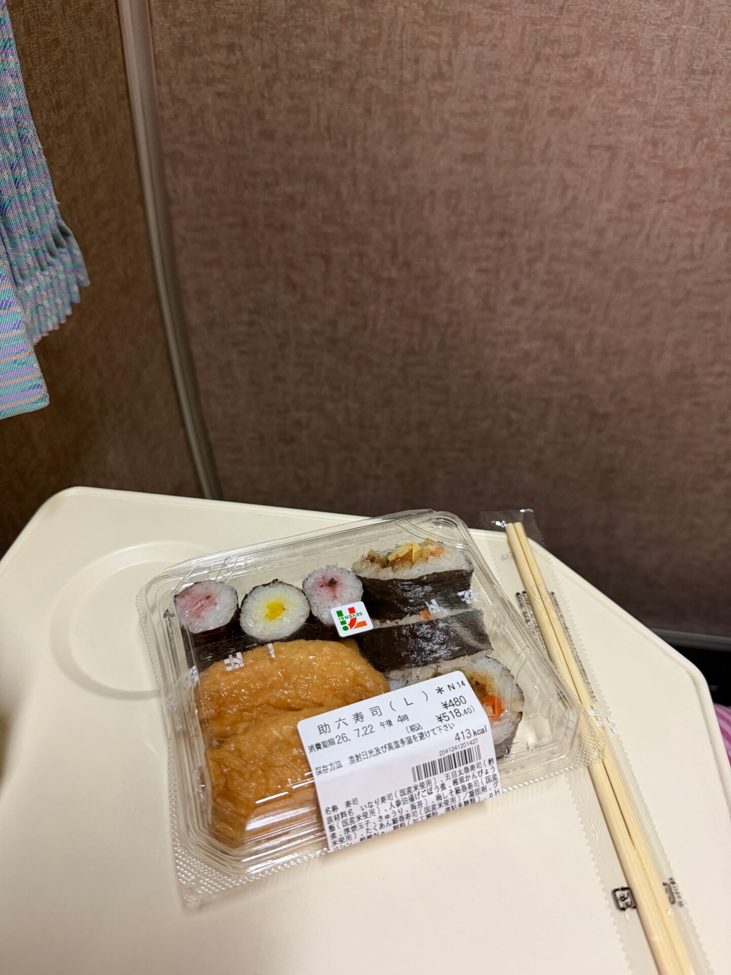 A packaged assortment of sushi from 7 Eleven in Japan sits on a tray with chopsticks. The selection includes inari sushi and several seaweed wrapped rolls with different fillings.