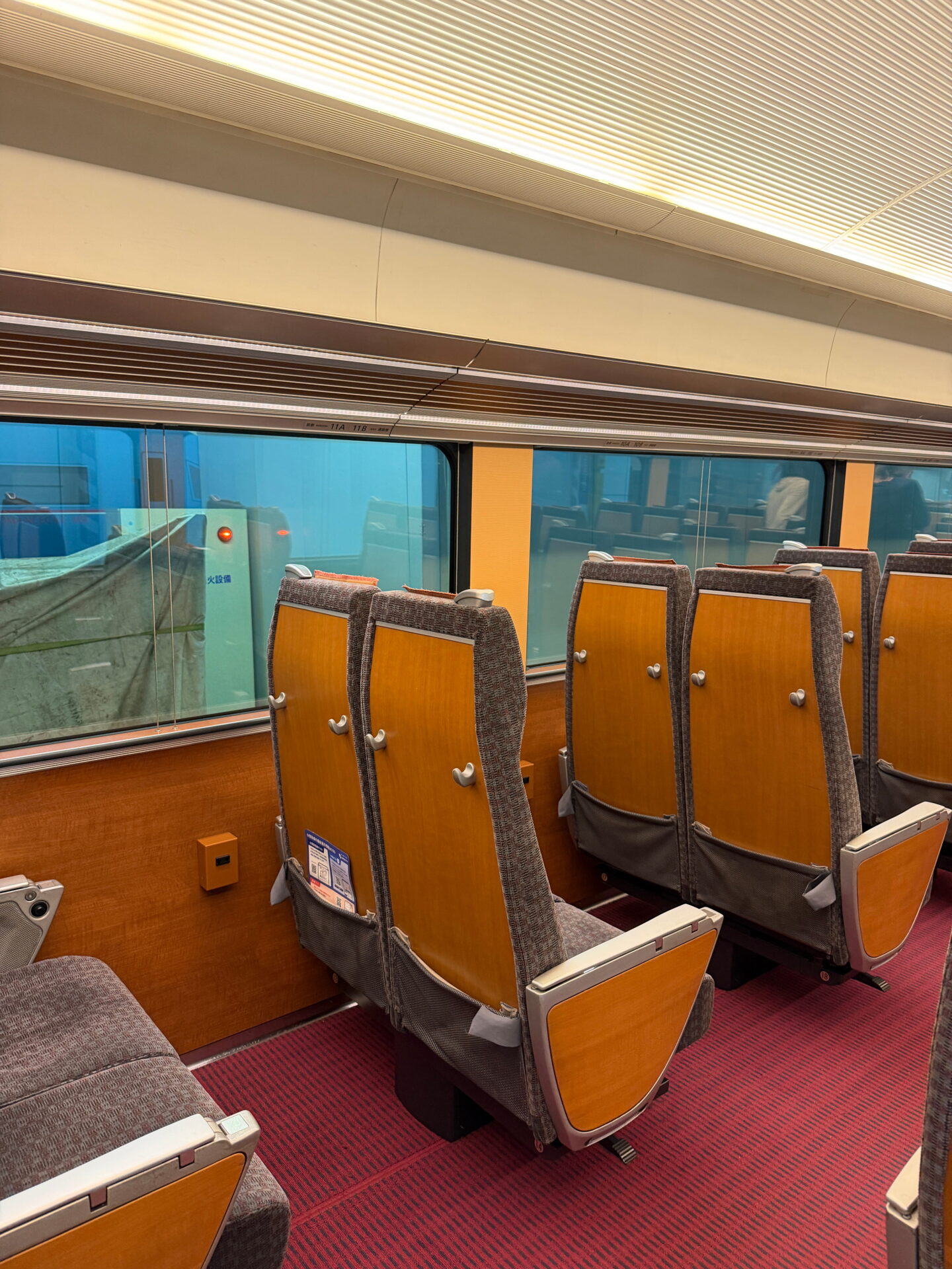 Rows of spacious seats with wooden backs and grey upholstery inside an Odakyu Romancecar train. Large windows run alongside the carriage for views during the journey to and from Hakone.