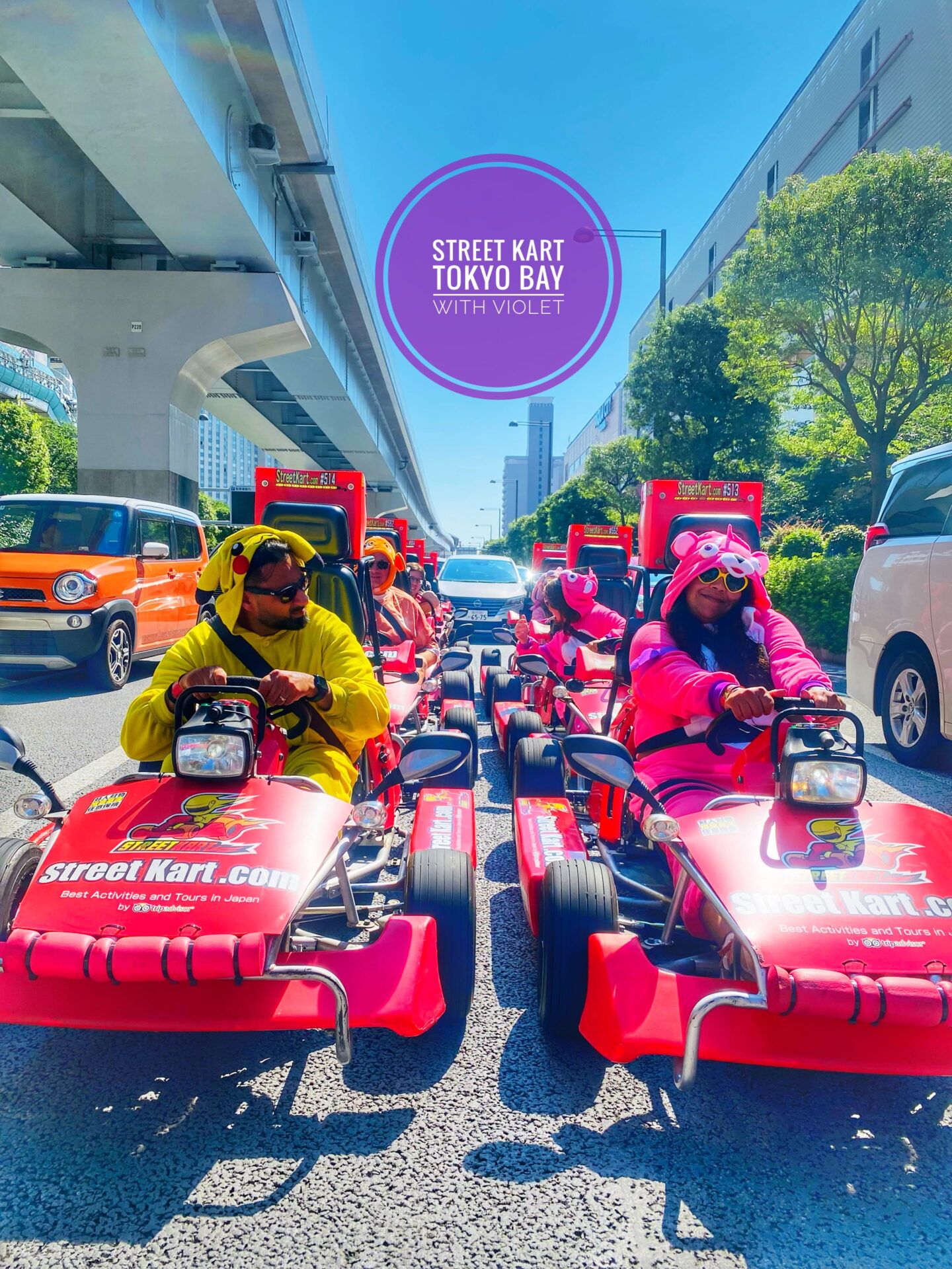 Nishi and Jass lead a group of costumed drivers in red Street Karts along a sunny Tokyo road. Jass wears a yellow Pikachu costume while Nishi wears a bright pink character costume and the graphic above them reads "Street Kart Tokyo Bay with Violet."