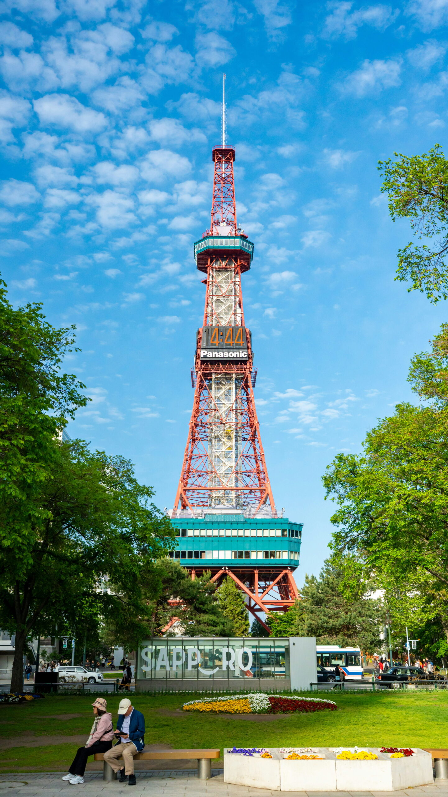 view of Sapporo TV Tower from Odori Park with an elderly couple sat on a bench in the park
